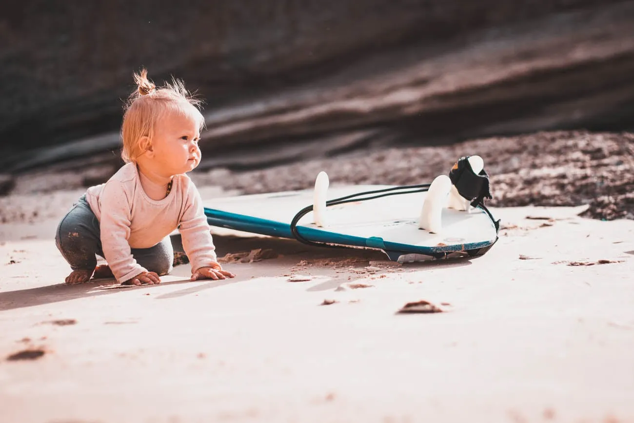 Baby am Strand mit Surfbrett